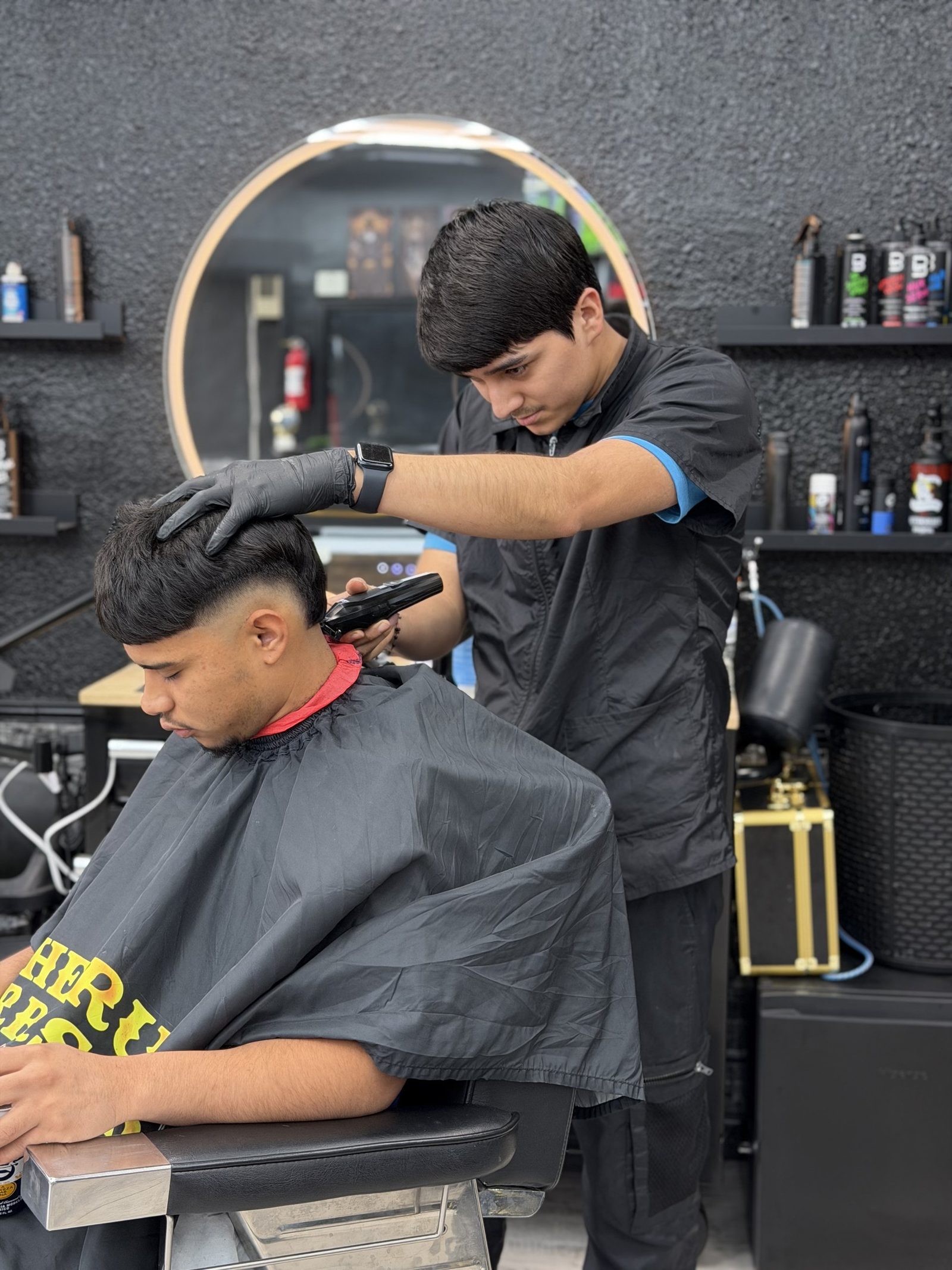 A barber giving a fresh fade — clipper work and dark wood tones.